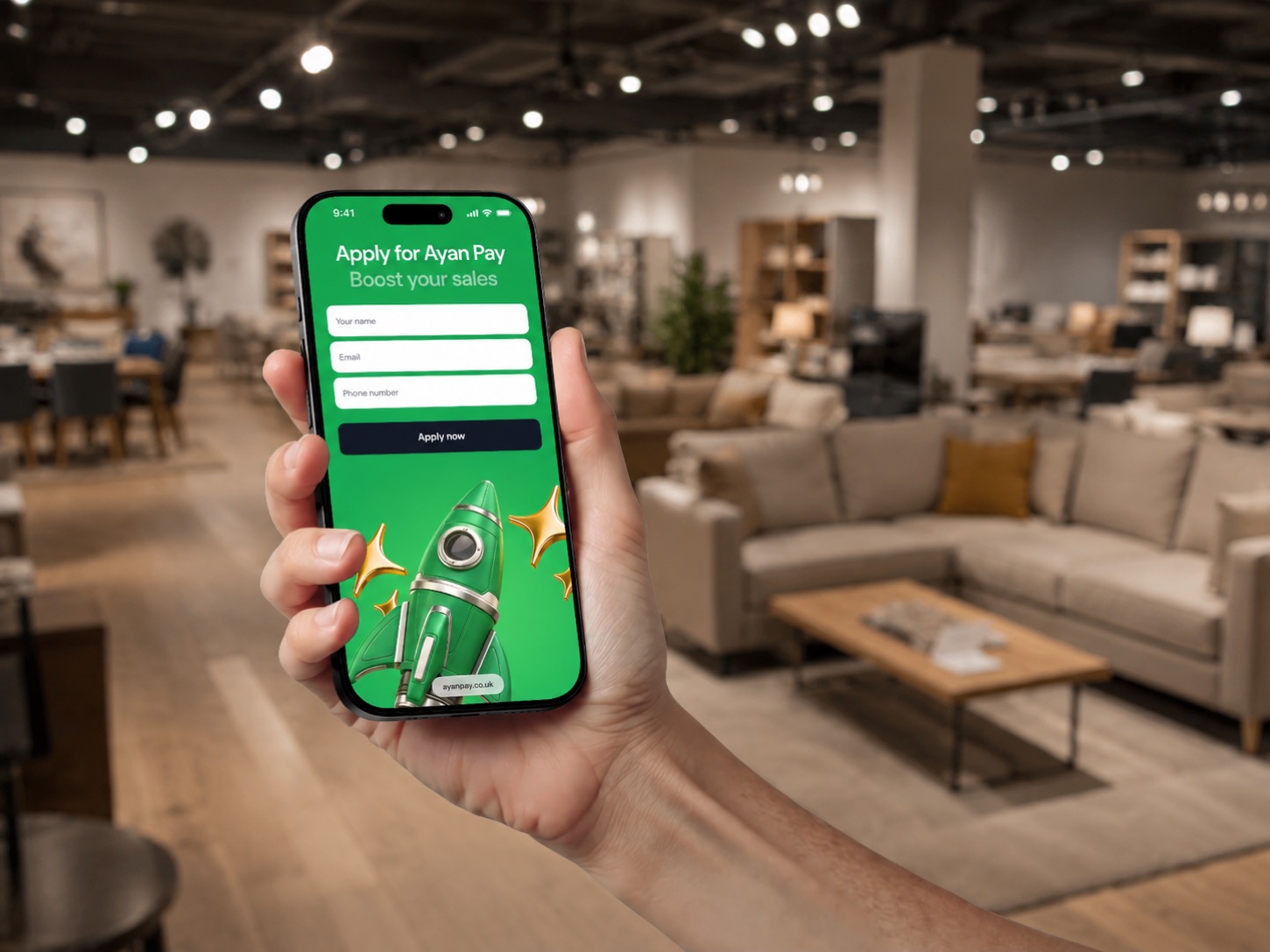 A hand holding a phone showing the Ayan Pay application form in a furniture showroom